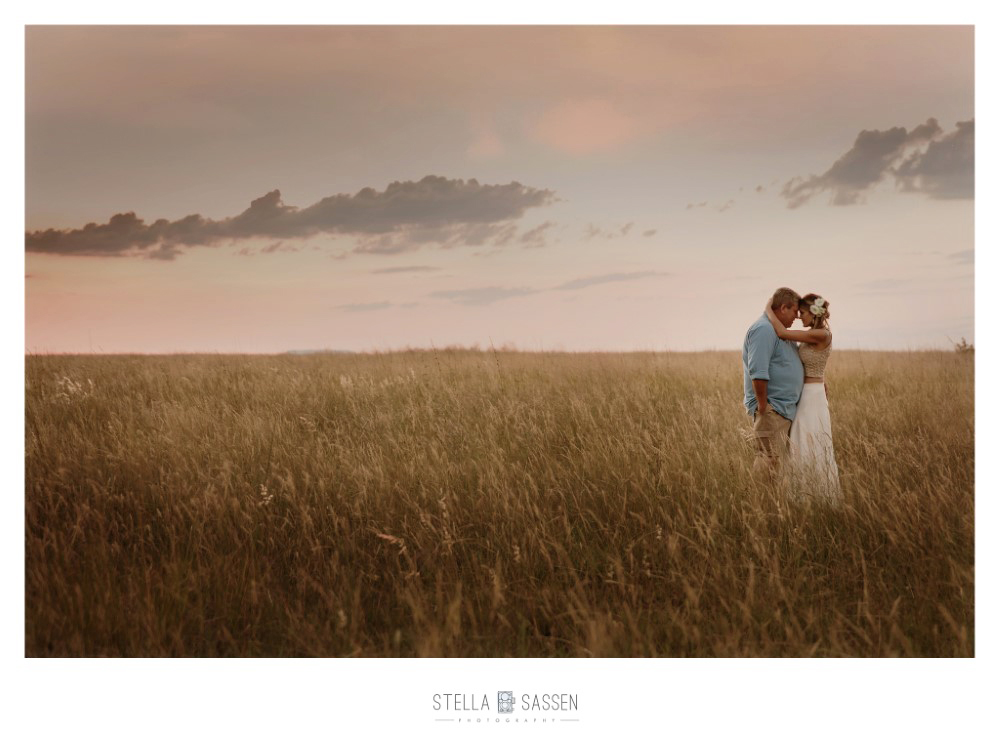 A bride and groom standing together forehead to forehead in a vast golden grassland at sunset, soft pink sky above them, during a bush wedding in South Africa.