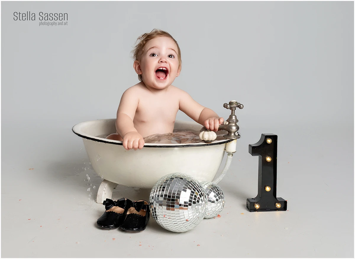 Baby girl toddler very excited for her bath after her cake smash, sitting in a cute little bath with a huge smile