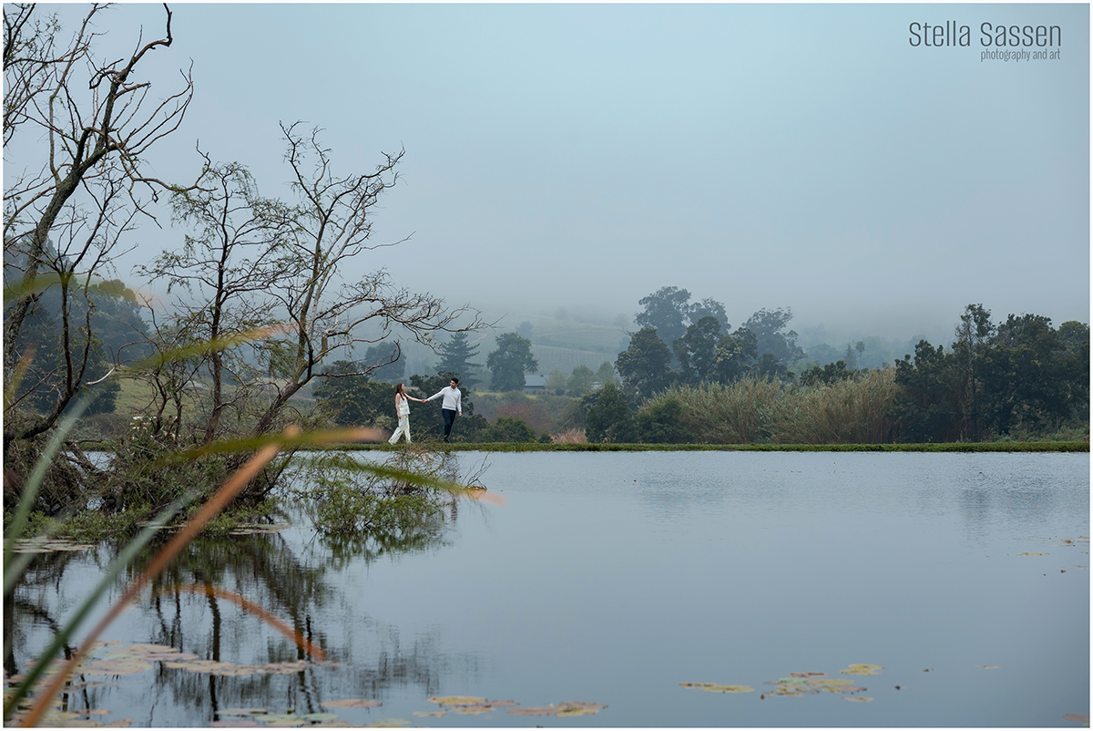 newly engaged couple walking on the edge of a lake holding hands on a misty day